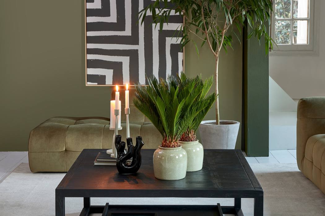 Riviera Maison Deko auf einem schwarzen Couchtisch mit Pflanzen, Bild Kerzenhaltern und Vase