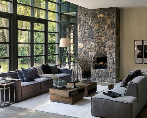 Wohnzimmer mit Sofas Riviera Maison Sofas einem gemauerten Kamin und zwei Couchtischen, sowie Deko