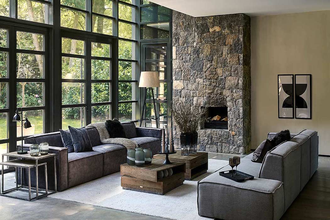 Wohnzimmer mit Sofas Riviera Maison Sofas einem gemauerten Kamin und zwei Couchtischen, sowie Deko